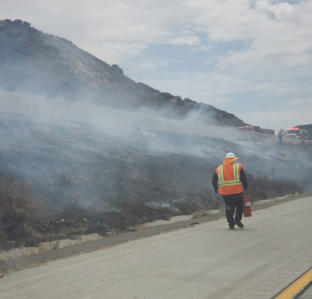 Worker wearing safety vest standing near brush fire on highway